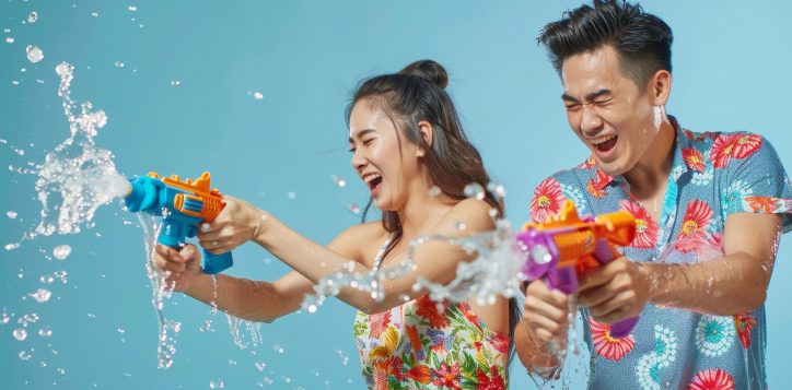 asian-couple-having-fun-playing-water-guns-wearing-colorful-patterned-summer-shirts-street-2